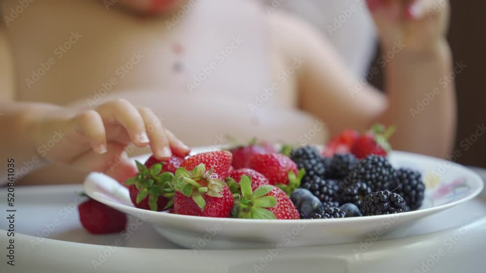 Baby boy eating berries for the first time, 1.5 year old toddler child sitting on highchair eatsstrawberries blackberries blueberries on the balcony in summer. Baby boy eating berries for the first time, 1.5 year old toddler child sitting on highchair eatsstrawberries blackberries blueberries on the balcony in summer.