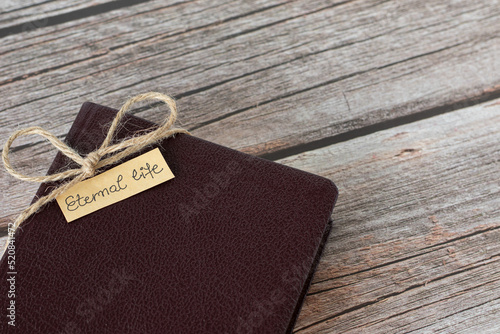 Foto Eternal life, handwritten text on a small note placed on a closed Holy Bible Book wrapped with vintage ribbon on a wooden table