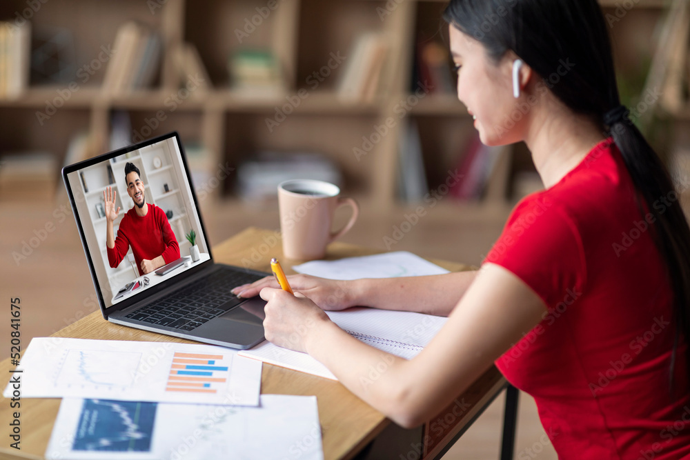 Smiling young asian girl student in headphones watch laptop with male teacher at screen, have video call and study