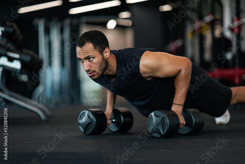 Fototapeta Naklejka Na Ścianę i Meble -  Muscular Black Man Making Dumbbell Push-Ups Exercise At Gym