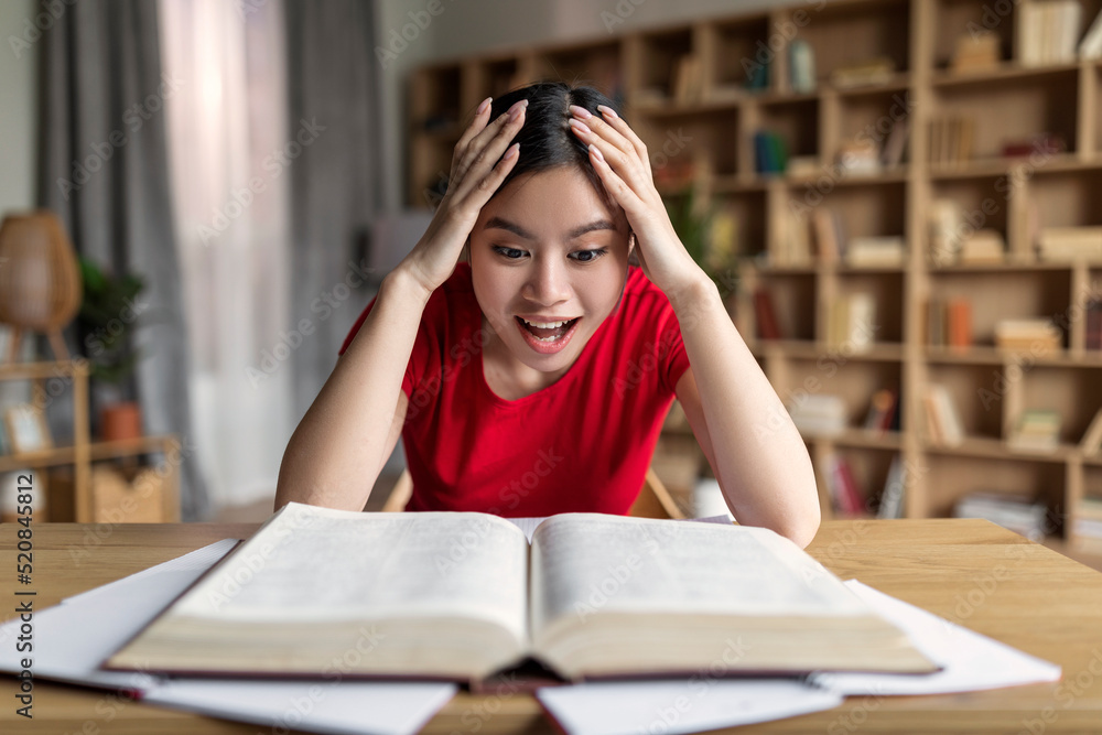 Happy shocked smart young korean female student looking at book, enjoy education at room interior Happy shocked smart young korean female student looking at book, enjoy education at room interior