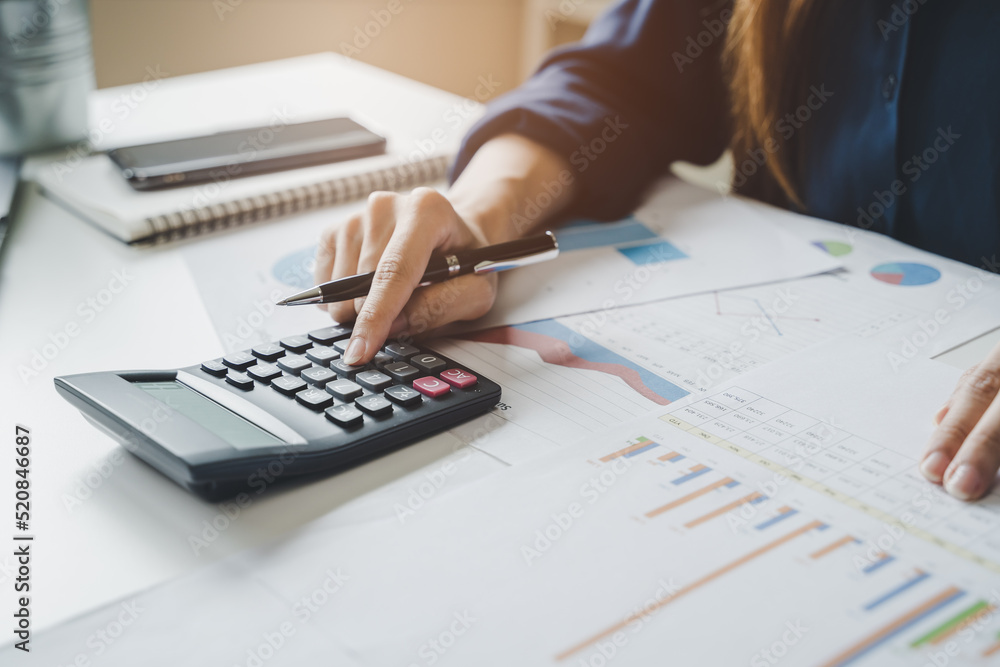 Women business people use calculators to calculate the company budget and income reports on the desk in the office. Women business people use calculators to calculate the company budget and income reports on the desk in the office.