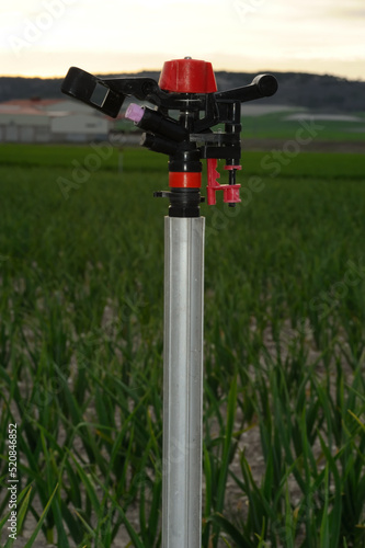 Close-up and low key vertical photograph of a sprinkler on farmland at sunset. Selective focus. Background blurred.