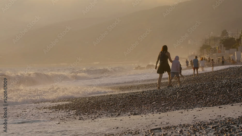 Waves on pebbled beach during sunset. Creative. Vacation Concept, people walking at the sea shore.