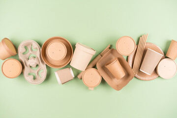 Eco paper utensils and disposable tableware, food containers, paper drinking straws and paper cups over light green background. Sustainable food packaging concept