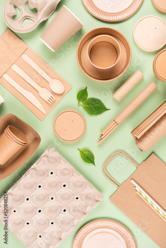 Vertical flat lay composition with eco tableware, paper utensils and wooden bamboo cutlery set over light green background. Sustainable food packaging concept