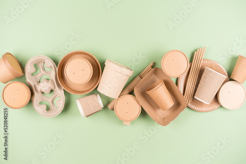 Eco paper utensils and disposable tableware, food containers, paper drinking straws and paper cups over light green background. Sustainable food packaging concept
