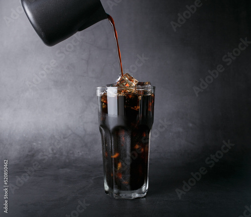 Poured coffee of ice americano coffee into a transparent glass on  black background studio photo