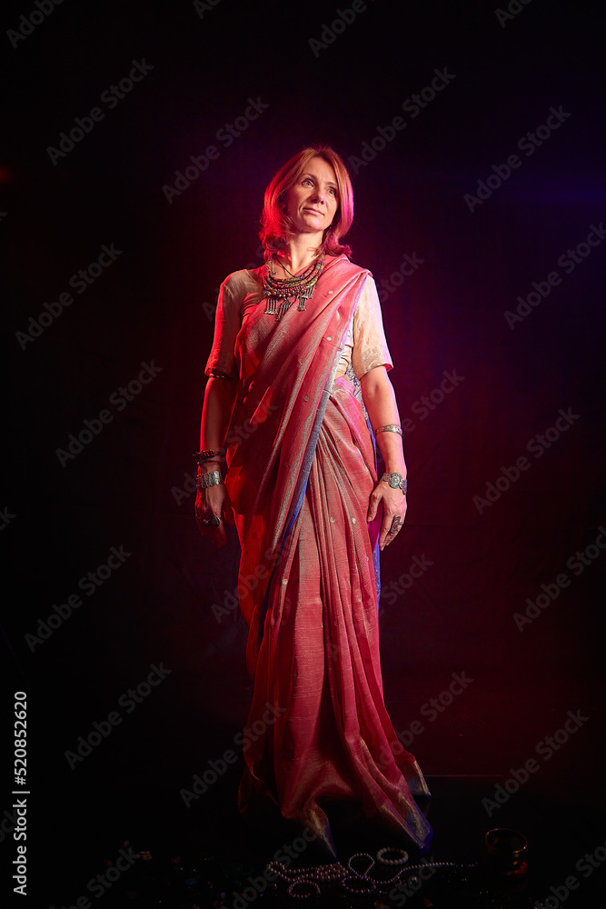 A beautiful European woman in a traditional Indian sari on a black background. Girl model posing in the studio