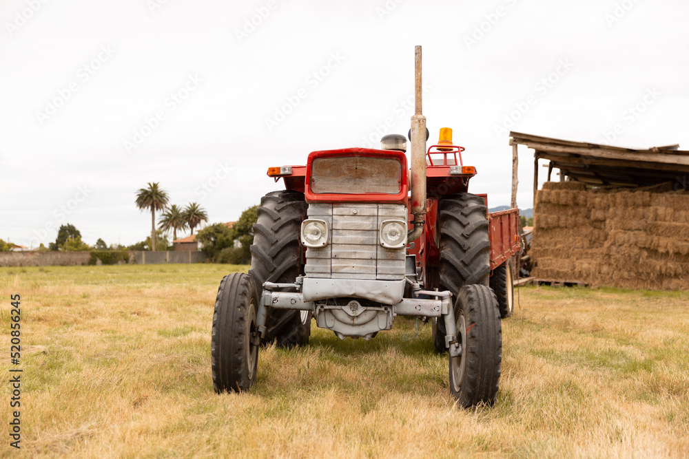 Front view of a tractor standing in a crop field. The day is cloudy. Concept of agriculture and rural life. Front view of a tractor standing in a crop field. The day is cloudy. Concept of agriculture and rural life.