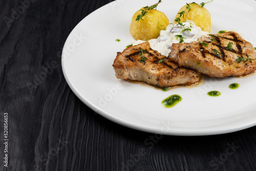 Grilled pork meat with mushroom sauce and potato on white plate on wooden black background