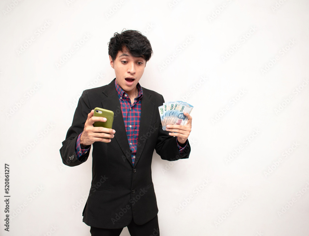 Hombre joven sorprendido sosteniendo algunos billetes y un telefono inteligente sobre un fondo blanco aislado Hombre joven sorprendido sosteniendo algunos billetes y un telefono inteligente sobre un fondo blanco aislado
