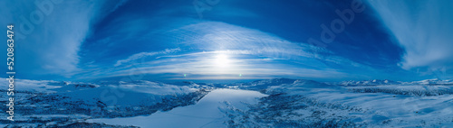 Aerial panoramic sunset over over Norwegian snowy winter mountains with frozen lake. Clear blue skies. Krutvatnet lake, Norway