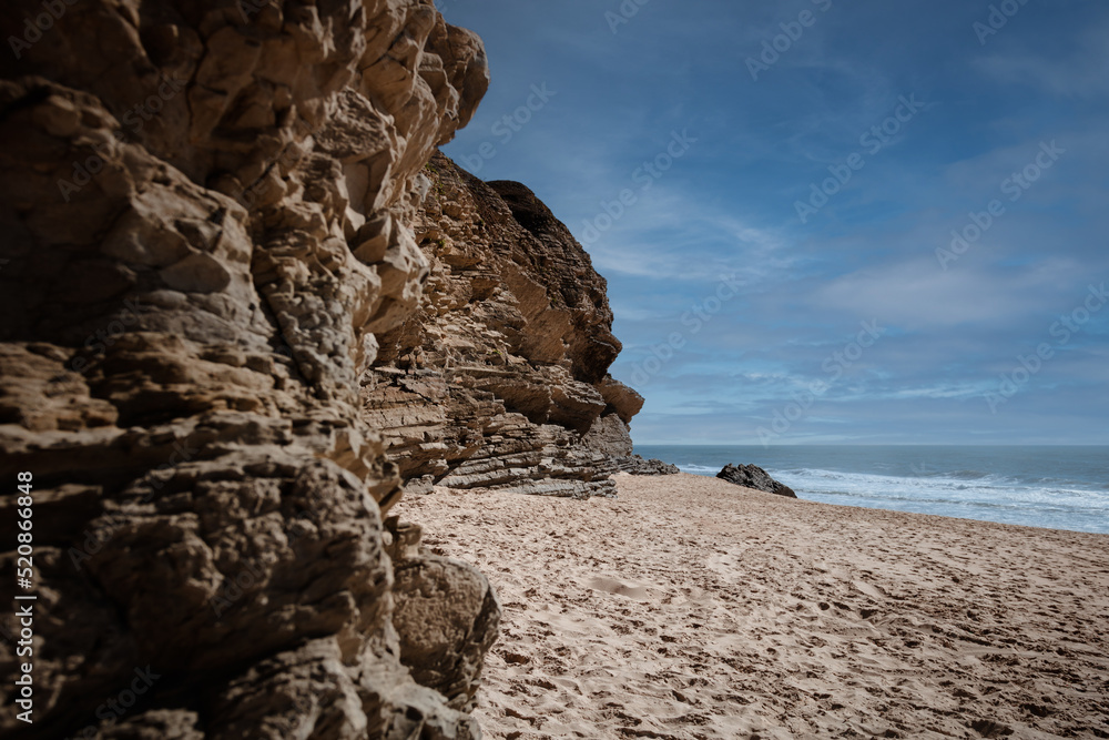 Fototapeta premium Praia da Murtinheira in Quiaios, Portugal, a quiet and wild beach away from the crowds. Close-up of rocky shore, sand and blue sky. Landscape photography