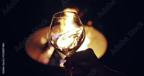 Tasting white wine at night. Glass of white wine slightly shaking against camp fire background. Winemaking in France, Provance. Slow motion shot, 4K