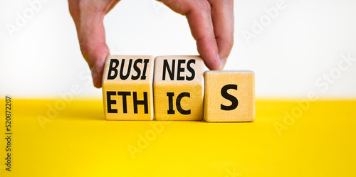 Business ethics symbol. Concept words Business ethics on wooden blocks. Businessman hand change words business on ethics. Beautiful yellow table white background. Business ethics concept. Copy space.