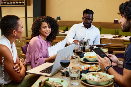 The business partners are having business lunch in a restaurant and looking at documents and laptops.