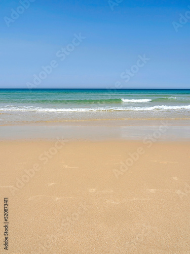Picturesque beach scenery on the coast of Cadiz, Spain. Orange sand, turquoise sea with waves and foam, clear sky, vacation, summer, relax.