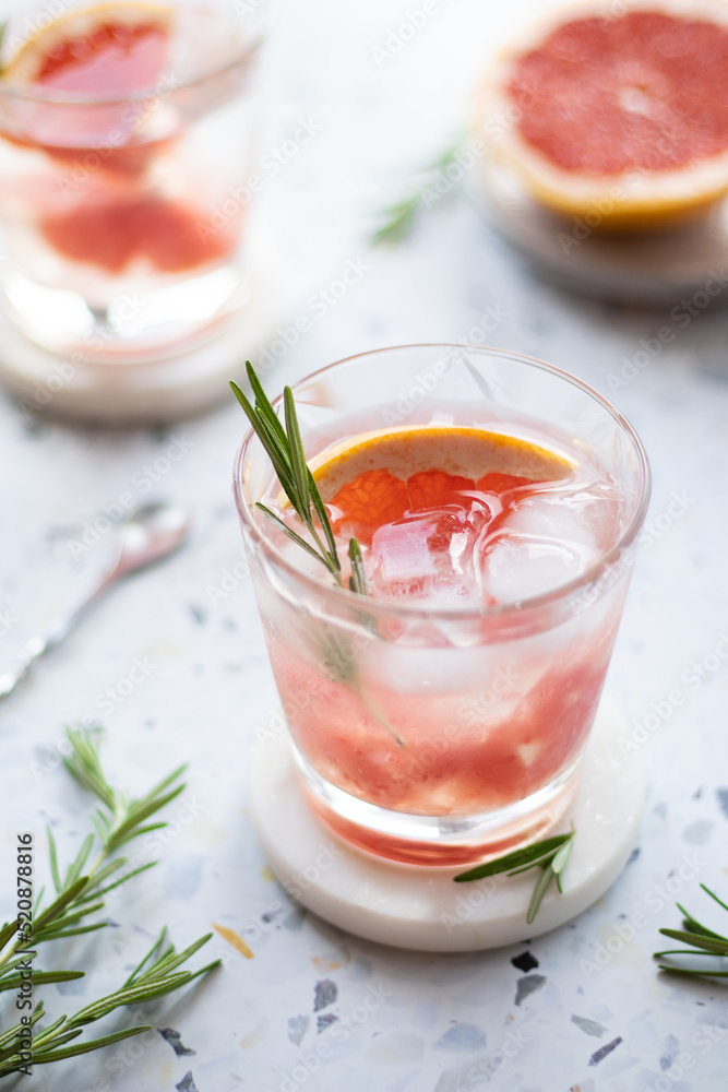 Grapefruit lemonade in a glass with ice cubes and rosemary. Summer cold drink on terrazzo background Grapefruit lemonade in a glass with ice cubes and rosemary. Summer cold drink on terrazzo background