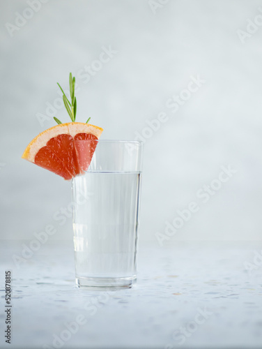 High glass of water decorated oiece of grapefruit and branch of rosemary. Terrazzo table, gray background. Copy space photo