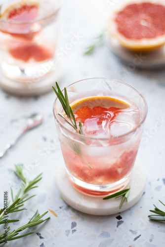 Grapefruit lemonade in a glass with ice cubes and rosemary. Summer cold drink on terrazzo background