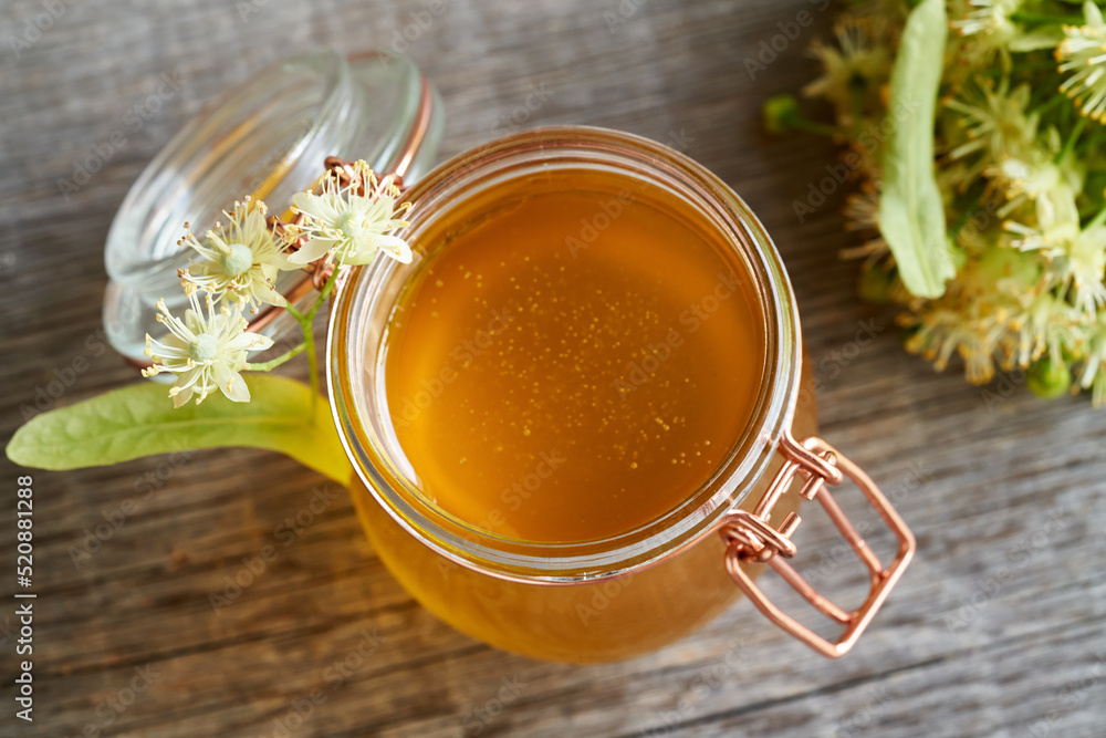 A jar of honey with fresh linden flowers, close up A jar of honey with fresh linden flowers, close up