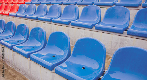 Empty bleacher in sports stadium in rainy weather. Colored wet seats in street stadium. It's raining. Close up.