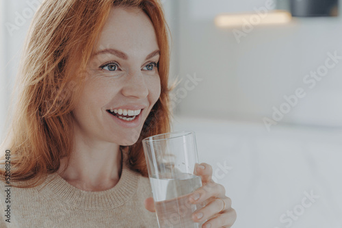 Ginger woman drinks pure water from glass enjoys refreshing drink