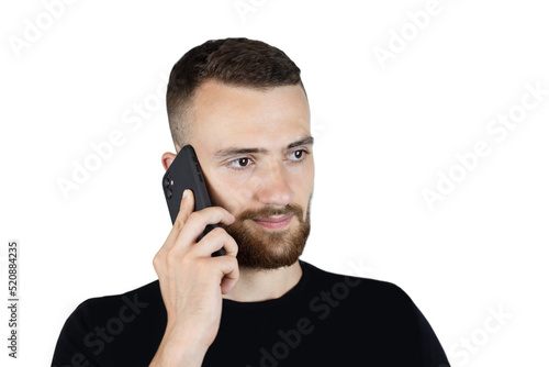 A young man in a black t-shirt and with a beard on a white background is talking on the phone and smiling, he often talks on the phone with his girlfriend and is happy about it