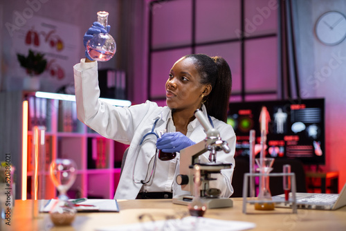 Scientific innovations. Positive smart enthusiastic african american woman scientist looking at the test tubes and smiling while developing a vaccine.