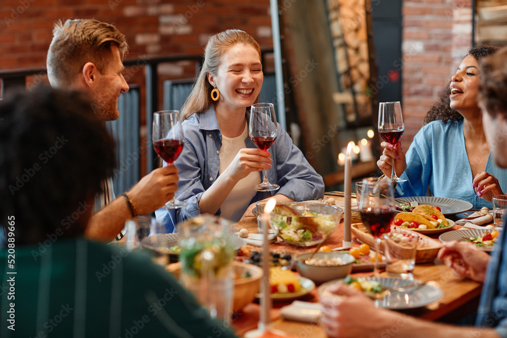 Portrait of young woman laughing happily during dinner party with friends in cozy setting