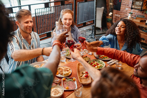 Diverse group of young people toasting with wine glasses while celebrating dinner party together, copy space
