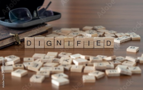 dignified word or concept represented by wooden letter tiles on a wooden table with glasses and a book photo