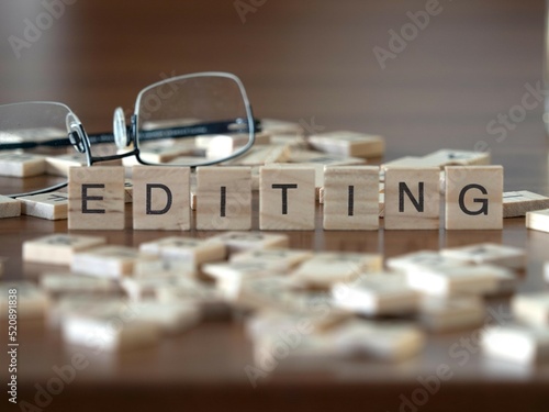 editing word or concept represented by wooden letter tiles on a wooden table with glasses and a book photo
