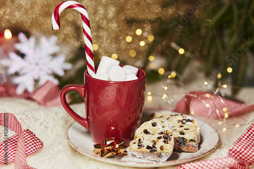 Hot drink in red cup with marshmallow and Christmas stollen - traditional holidays bread, gingerbread cookies, candy cone stick. Festive holidays Christmas background. Christmas food. Merry tradition. photo