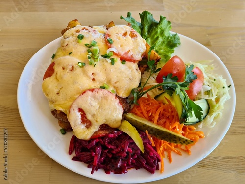 French meat with melted cheese and fresh vegetable salad on white plate