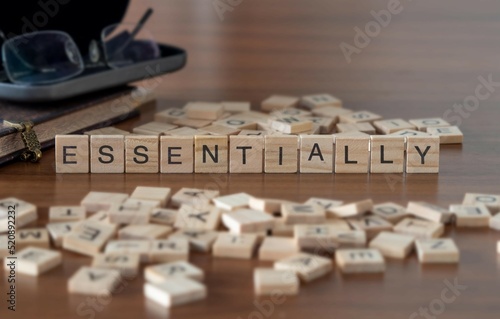 essentially word or concept represented by wooden letter tiles on a wooden table with glasses and a book