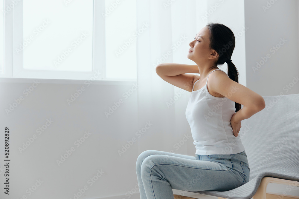 Back pain. Suffering from osteochondrosis after long study work pretty young Asian woman touching painful lower back at home interior living room. Injuries Poor health Illness concept. Cool offer Back pain. Suffering from osteochondrosis after long study work pretty young Asian woman touching painful lower back at home interior living room. Injuries Poor health Illness concept. Cool offer