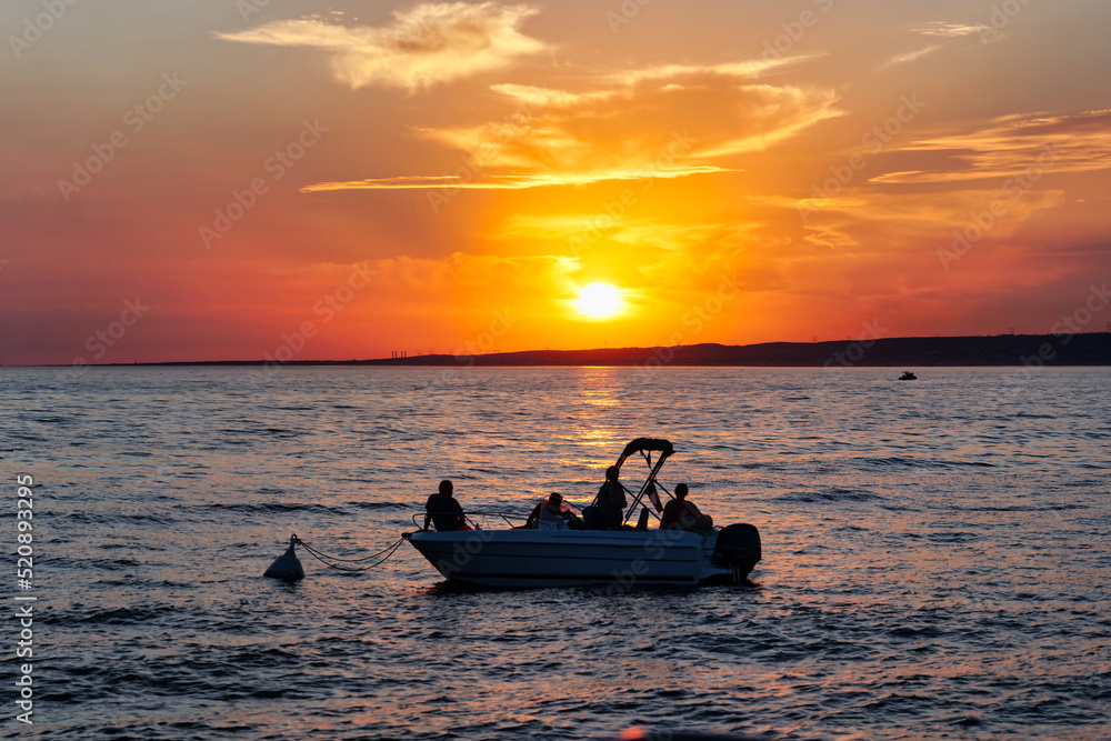 Small boat in front of the sunset. People enjoy the sunset on a boat. Boat at the ocean during golden hour.   A boat anchored in a bay around Marseille, France. 