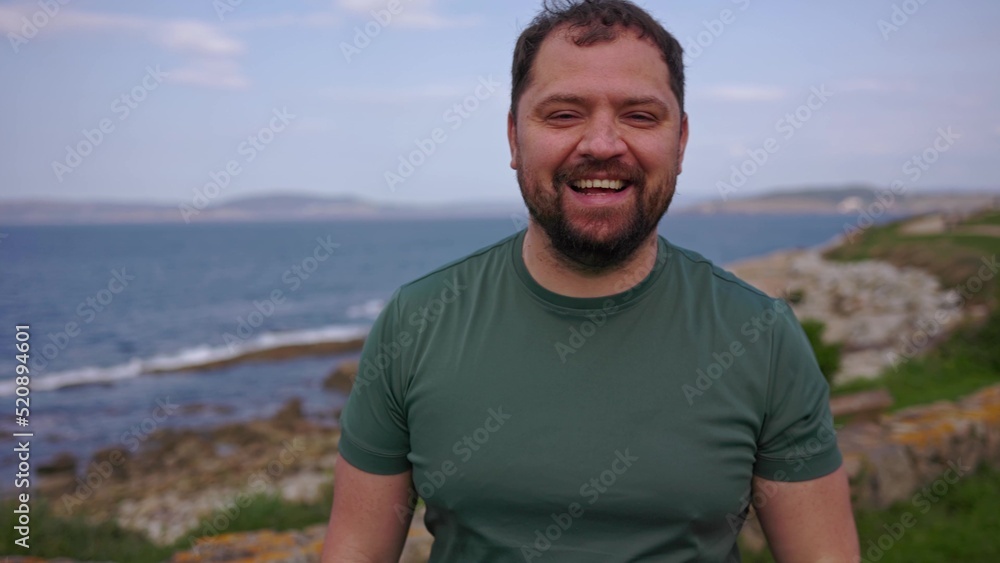 A man laughs and touches his beard in nature.