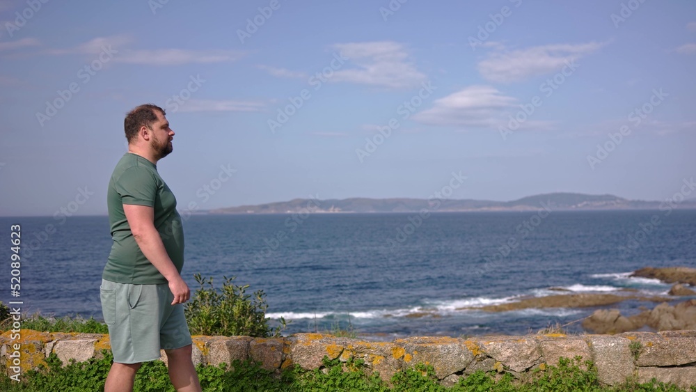 A man walks along the ocean and looks into the distance.