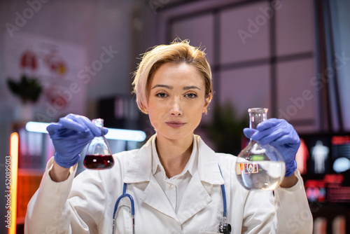 Focus on test tube. Scientific innovations. Positive smart enthusiastic woman scientist looking at the test tubes and smiling while developing a vaccine.