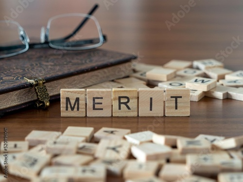 merit word or concept represented by wooden letter tiles on a wooden table with glasses and a book photo