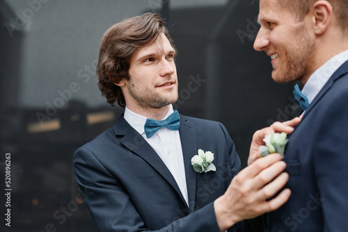 Portrait of smiling young man fixing grooms boutonniere during wedding ceremony, same sex marriage concept photo