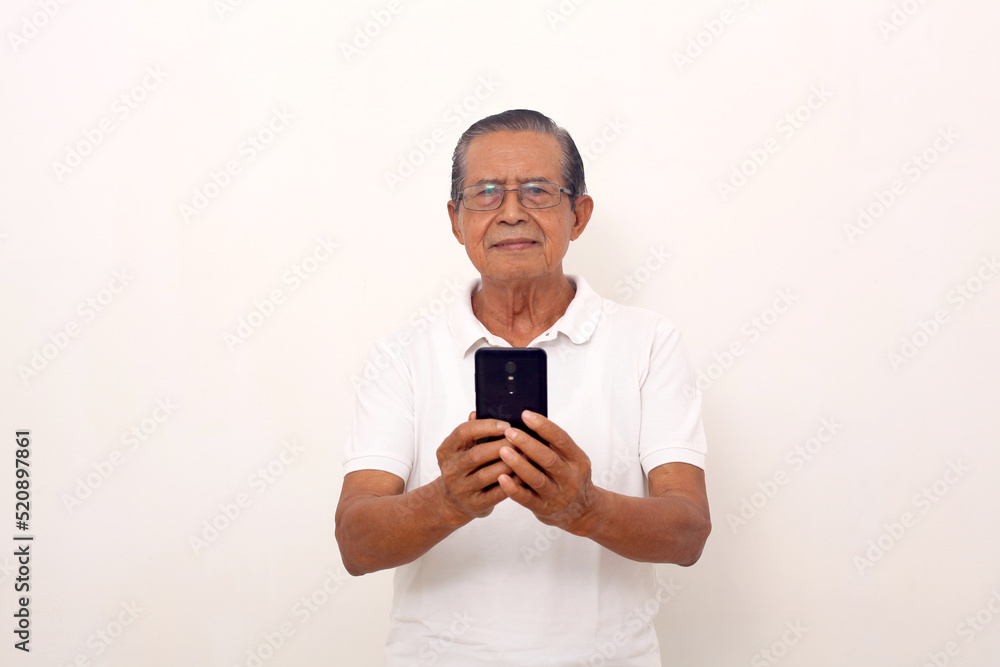 Calm elderly asian man standing while holding a cell phone. Isolated on white background Calm elderly asian man standing while holding a cell phone. Isolated on white background