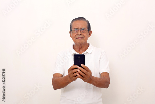 Calm elderly asian man standing while holding a cell phone. Isolated on white background © SetianingDyah