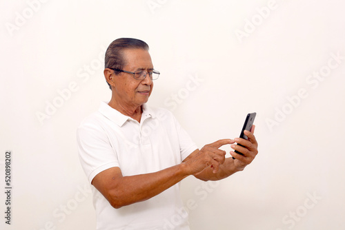 Happy asian old man standing while pointing or using a cell phone. Isolated on white. © SetianingDyah