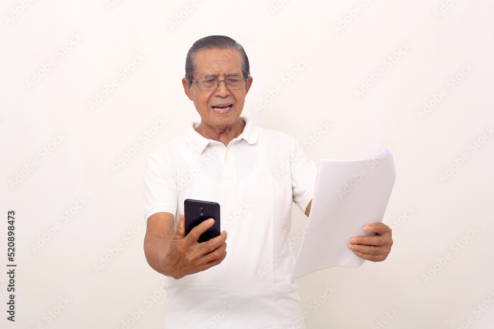 Surprised asian old man standing while holding cell phone and papers. Isolated on white background. Surprised asian old man standing while holding cell phone and papers. Isolated on white background.