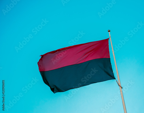 Red-black flag of Ukrainian nationalists, isolated on a blue sky background, close-up. Background of silk fabric fluttering in the air. photo