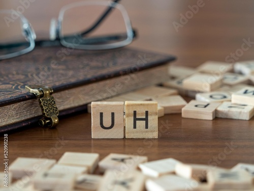 uh word or concept represented by wooden letter tiles on a wooden table with glasses and a book photo